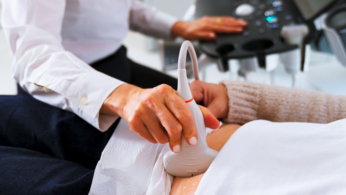 Clinician holding an ultrasound probe against a patient's abdomen during a private scan