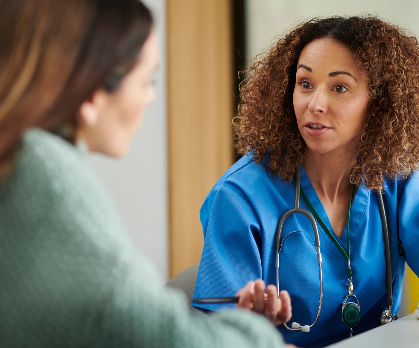 Female nurse in blue scrubs talking with a patient across a desk about what to expect from a hysteroscopy at Enigma Healthcare, Tarporley.