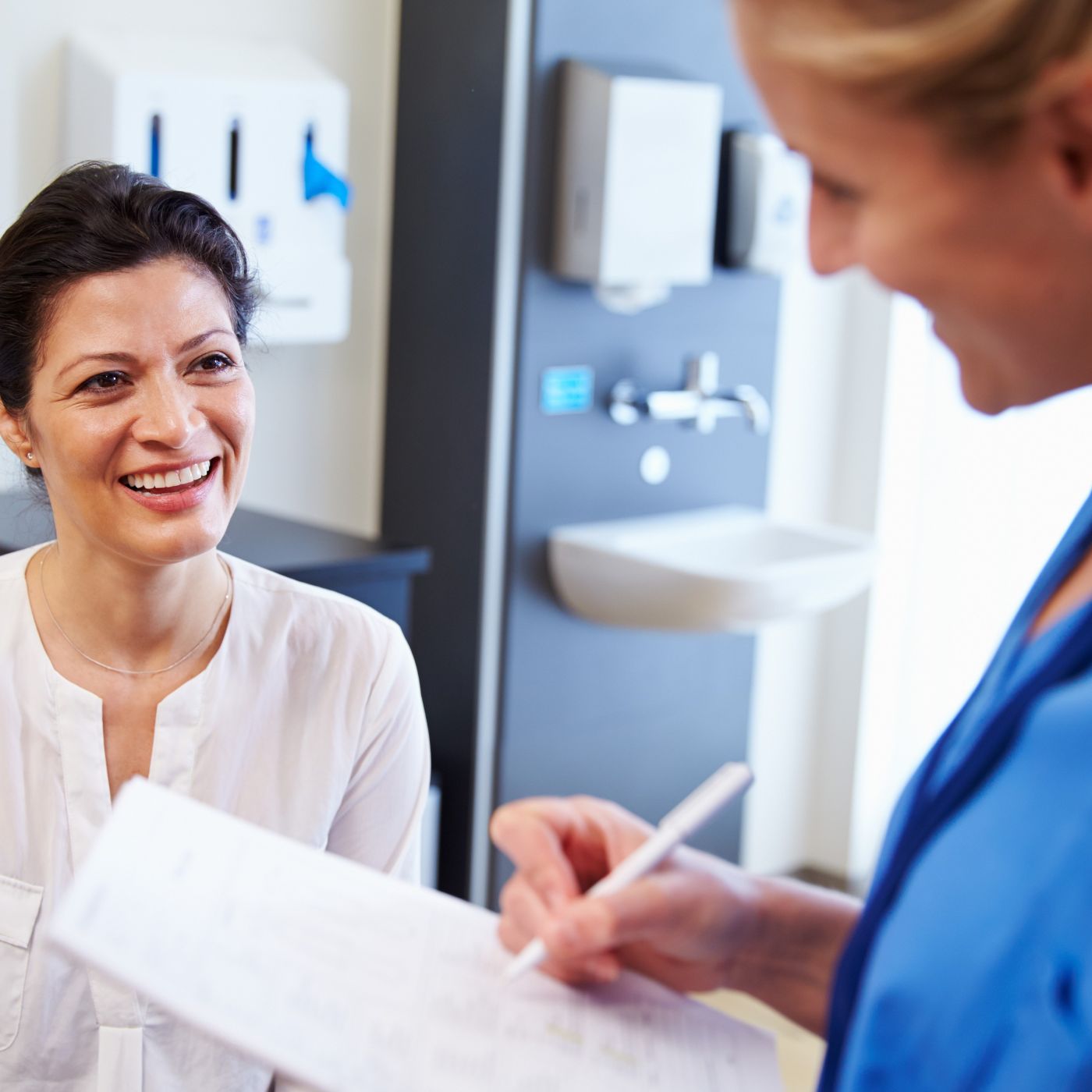 Smiling woman talking with a female clinician in blue scrubs during a consultation at Enigma Healthcare, Cheshire.