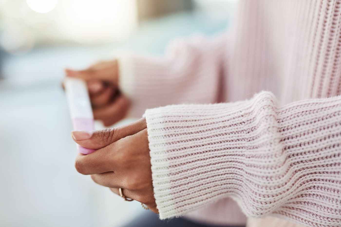 Close-up of a woman's hands in a soft pink jumper holding a test at home while awaiting fertility results from Enigma Healthcare, Tarporley.